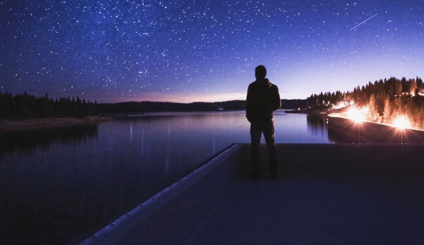 A man is standing on a dock looking at the stars.