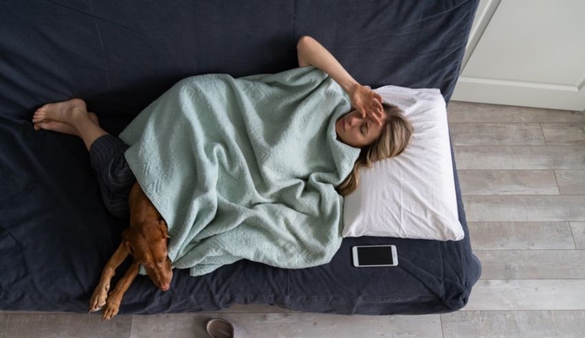 A woman laying on a bed with her dog under a blanket.