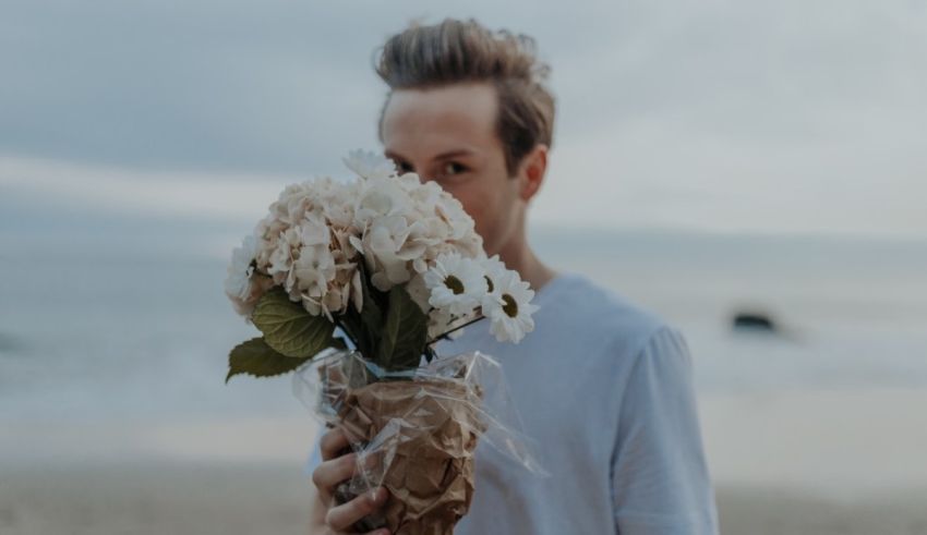A man holding a bouquet of flowers on the beach.