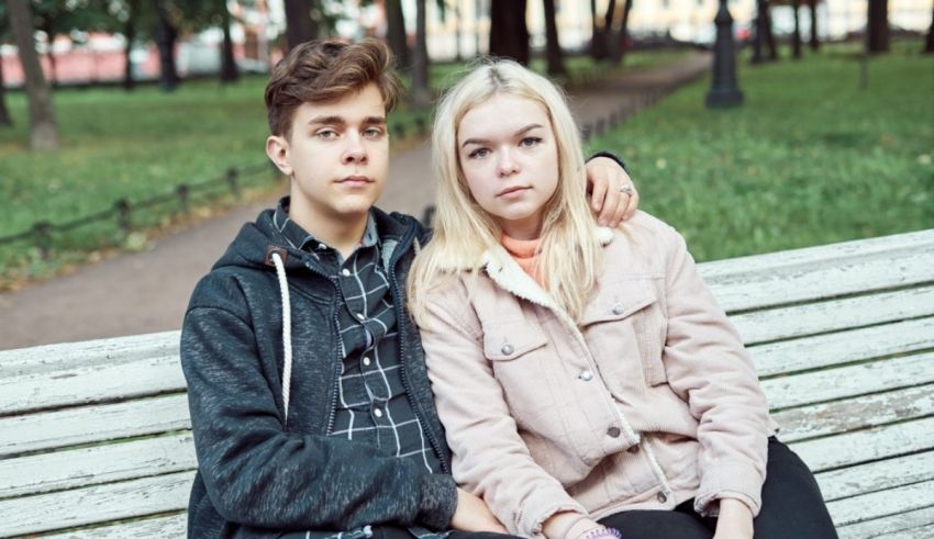 Two young people sitting on a bench in a park.