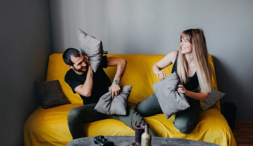 Man and woman playing with pillows on a yellow couch.