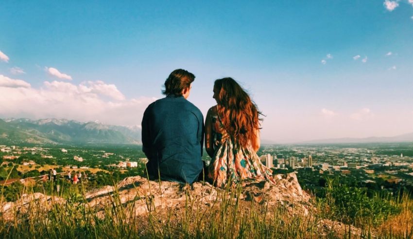 A couple sitting on top of a hill overlooking a city.