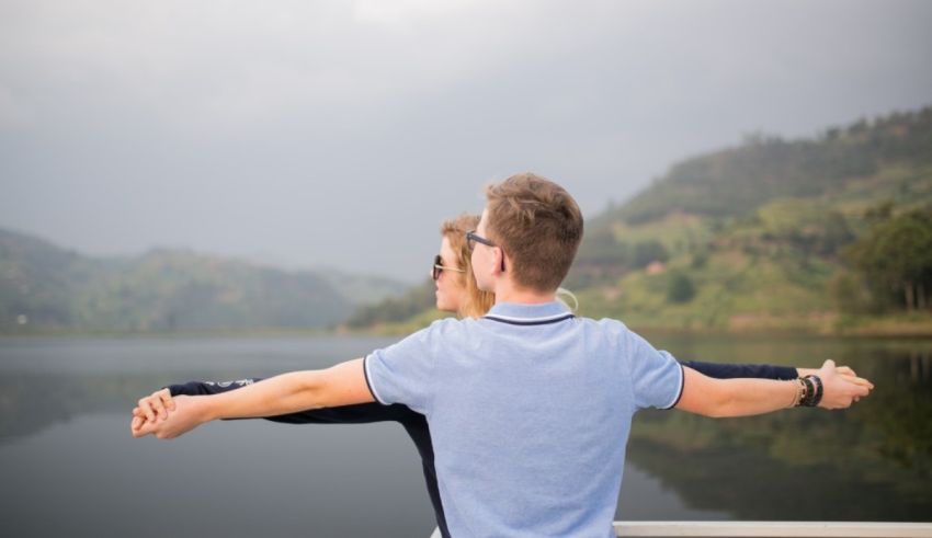 Young couple with arms outstretched on a boat overlooking a lake.