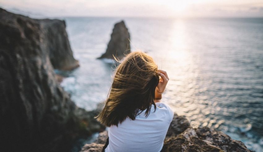 A woman sitting on a rock looking at the ocean.