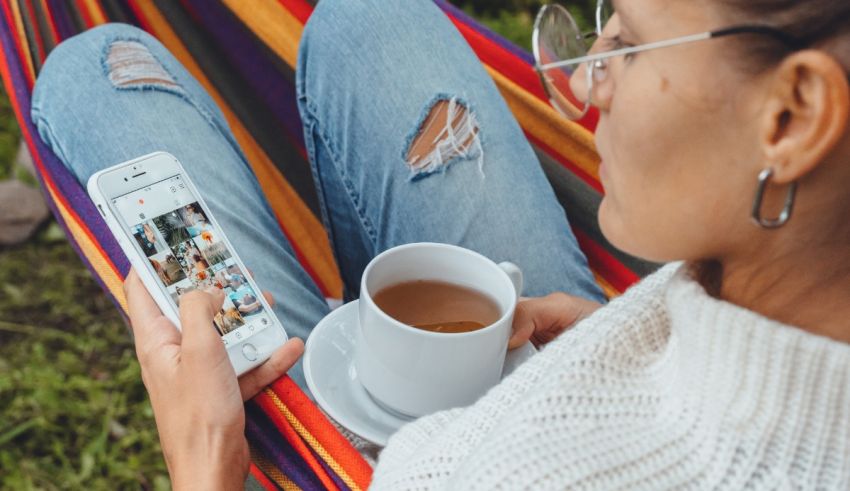 A woman is sitting in a hammock with her phone and a cup of coffee.