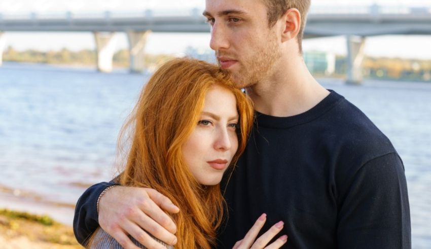 A man and woman hugging in front of a bridge.