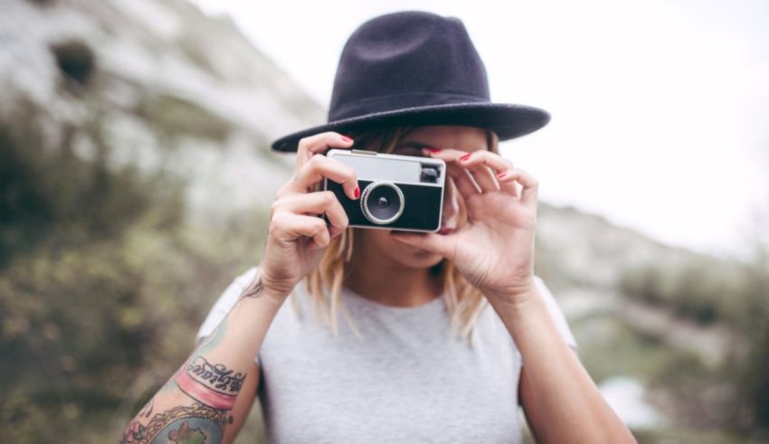 A woman with tattoos taking a picture with a camera.