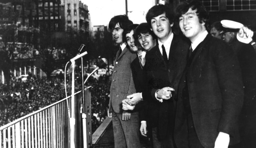 The beatles stand on a stage in front of a crowd.