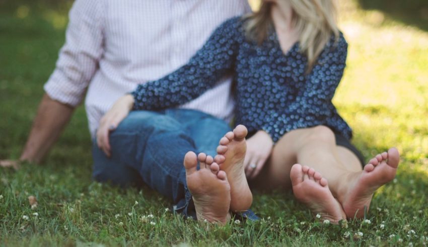 A couple sits on the grass with their feet together.