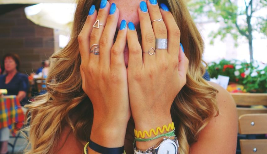 A woman with blue nails covering her face with her hands.