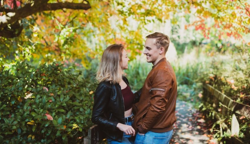 A couple standing in a park with autumn leaves in the background.