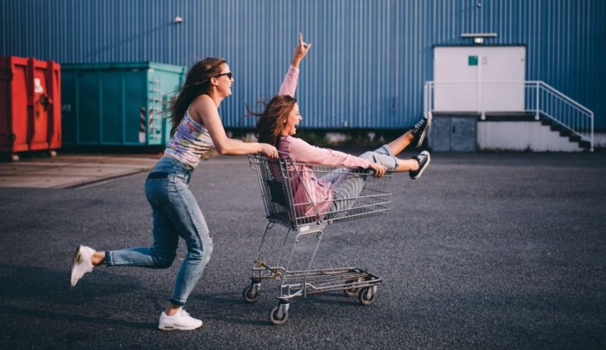 Two women pushing a shopping cart in a parking lot.