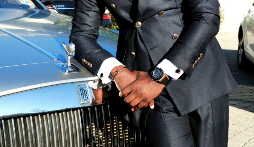 A man in a suit leaning against a rolls royce.