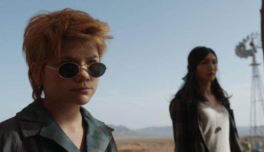 Two women in sunglasses standing next to a windmill in the desert.