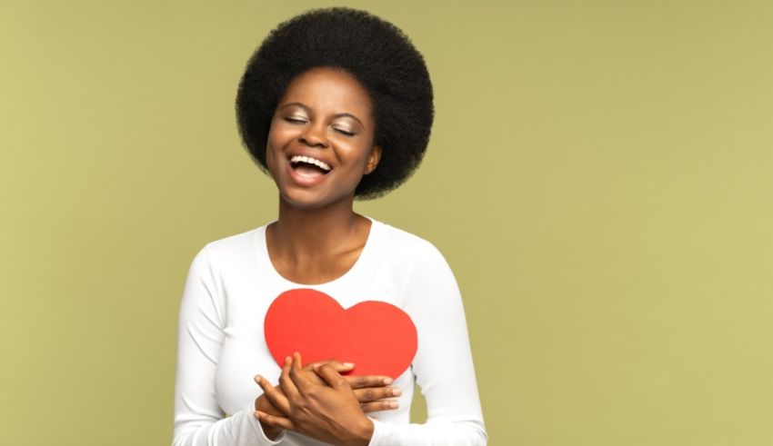 Young african american woman holding a red heart on a green background.