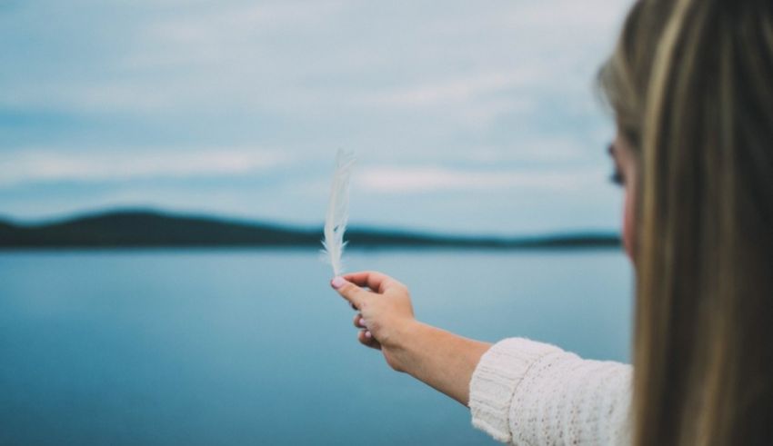 A woman holding a feather in front of a lake.