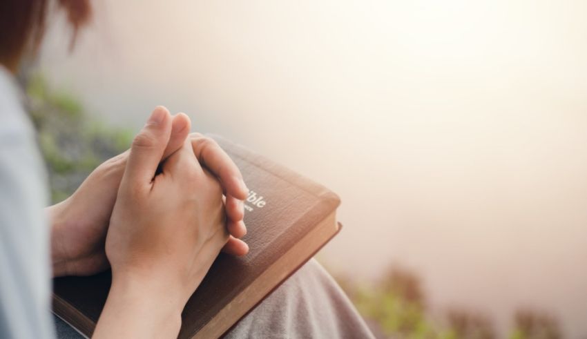 A woman praying with her hands on a bible.
