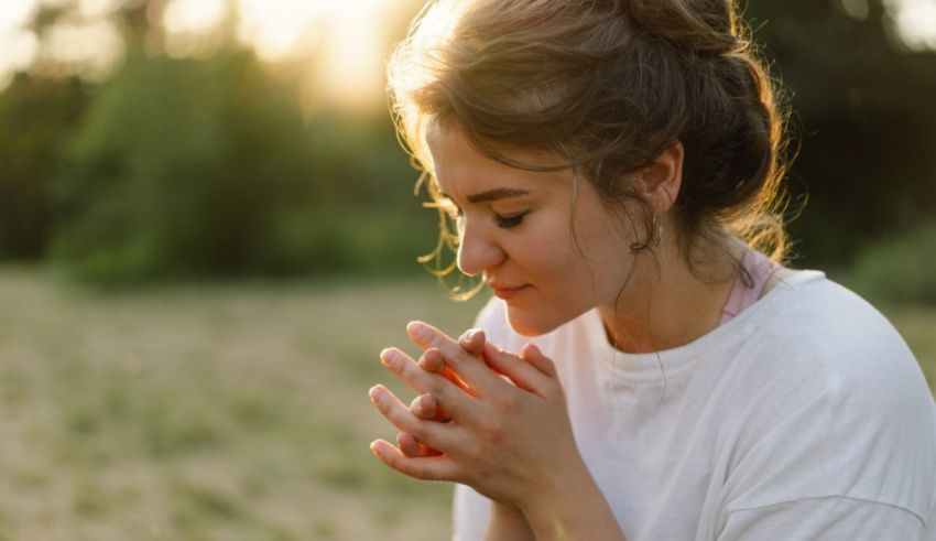 A young woman praying in a field at sunset.