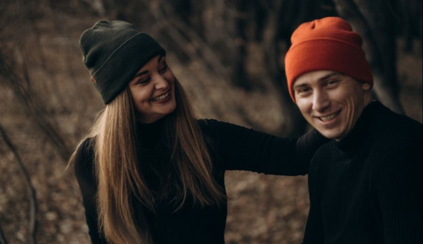A man and woman wearing beanie hats in the woods.