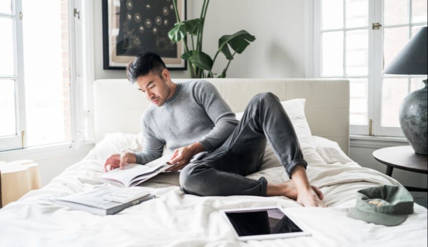 A man sitting on a bed reading a book.