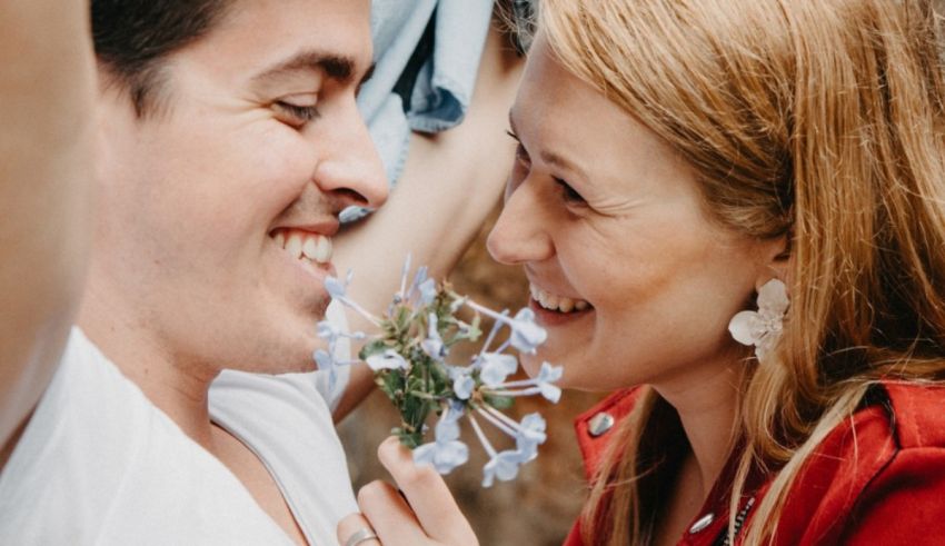 A man and woman are smiling while holding a bouquet of flowers.