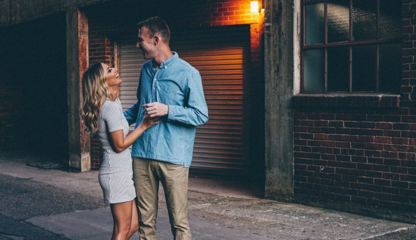 An engaged couple standing in front of a brick building at night.