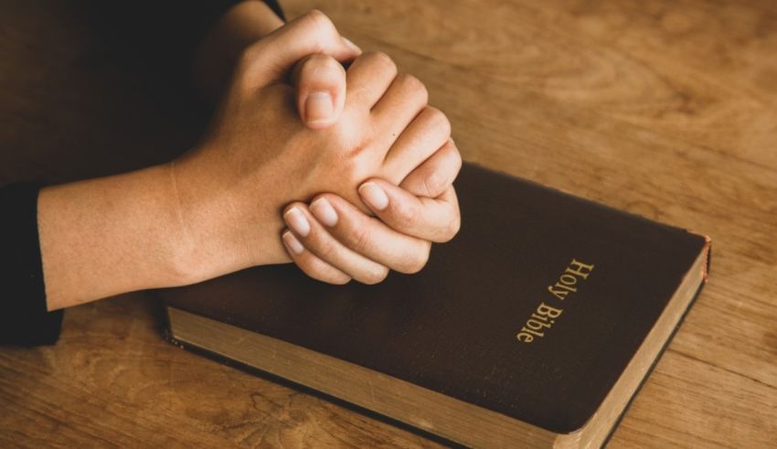 A woman's hands holding a bible on a wooden table.