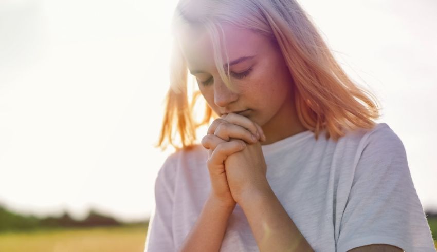 A young woman praying in a field.