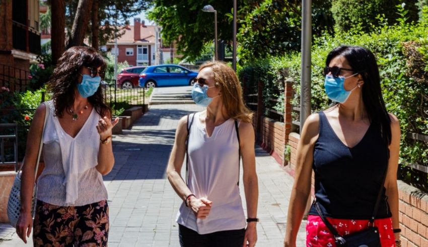 Three women wearing face masks walking down a sidewalk.