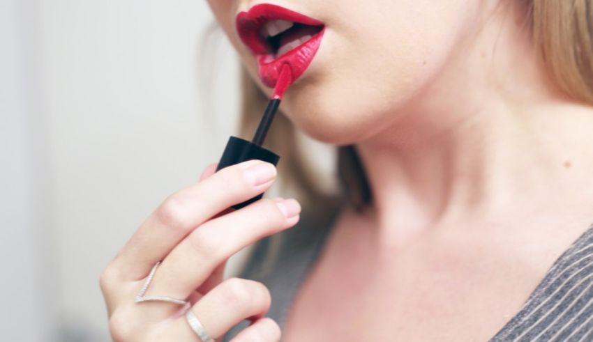A woman is putting lipstick on her lips.