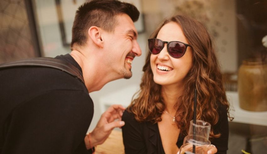 A man and woman are laughing while holding a glass of wine.