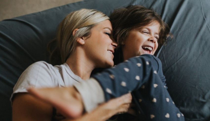 A mother and child laughing on a bed.