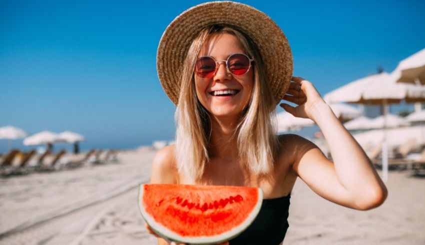 A woman holding a slice of watermelon on the beach.