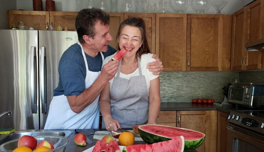 A man and woman preparing watermelon in the kitchen.