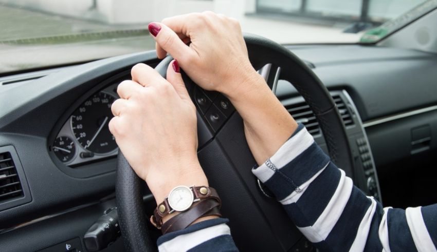 A woman is driving a car with her hands on the steering wheel.