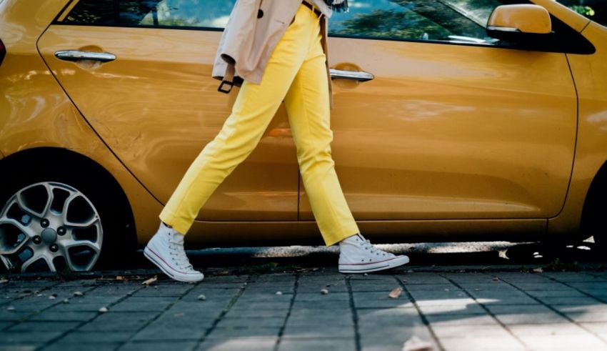 A woman in yellow pants is leaning against a yellow car.