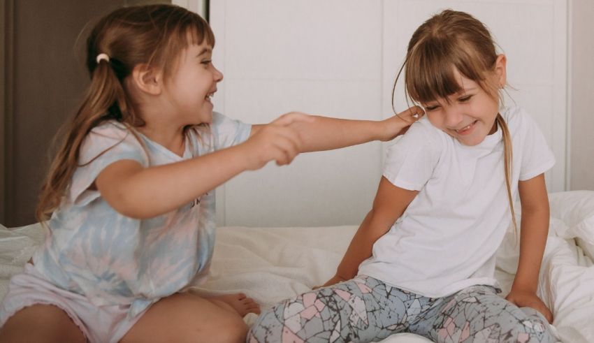 Two little girls sitting on a bed and playing with each other.