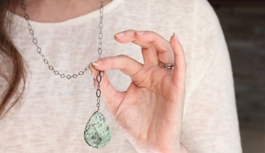 A woman holding up a necklace with a turquoise stone.