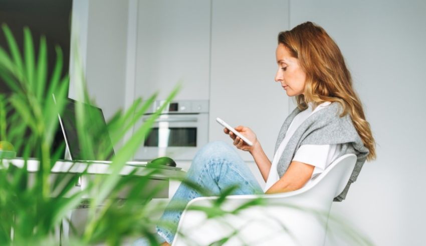 A woman is sitting in front of a plant while using her phone.
