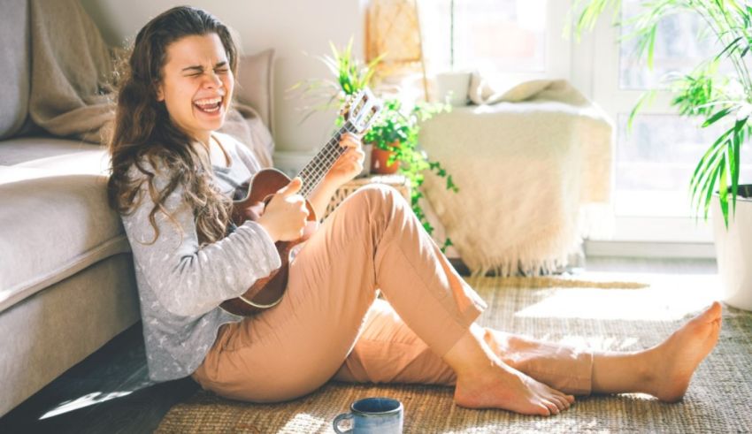 A young woman playing an ukulele on the floor at home.