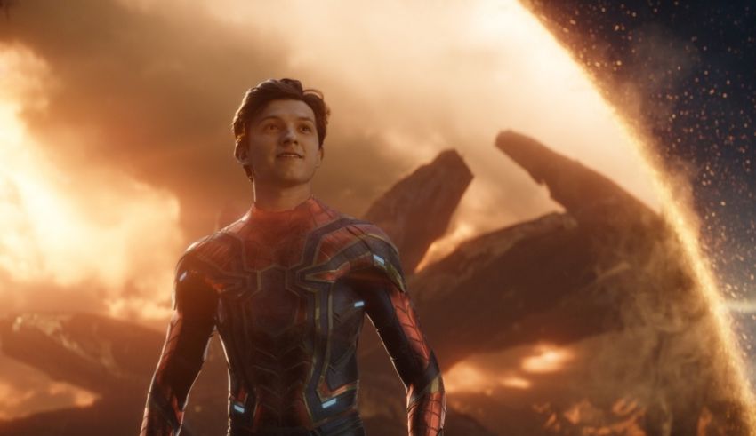 A man in a spider - man suit standing in front of an explosion.