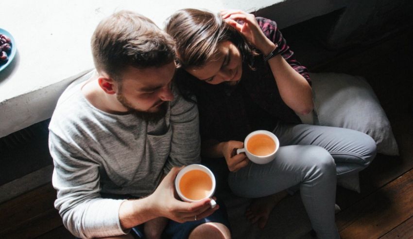A man and woman sitting on a window sill drinking tea.