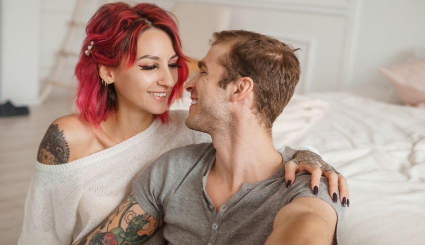 A man and woman with tattoos sitting on a bed.