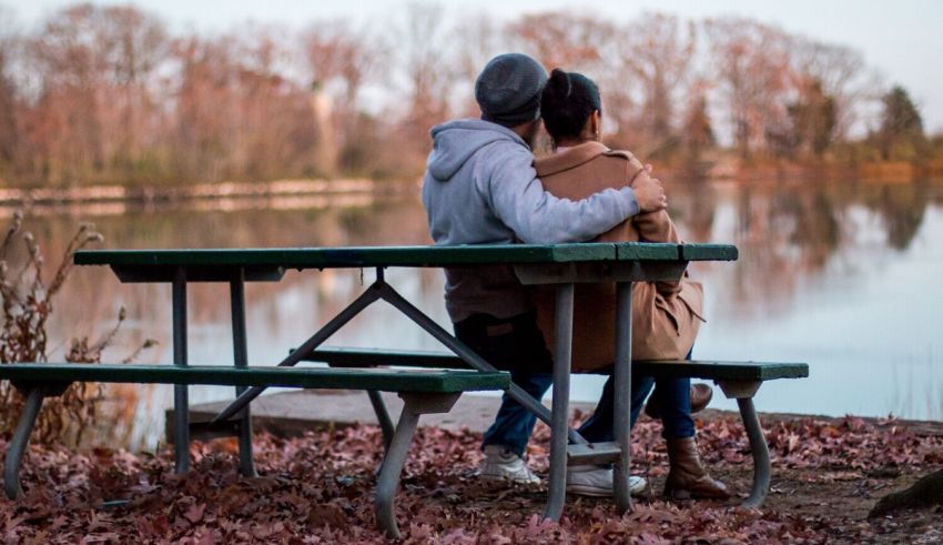A couple sitting at a picnic table near a lake.