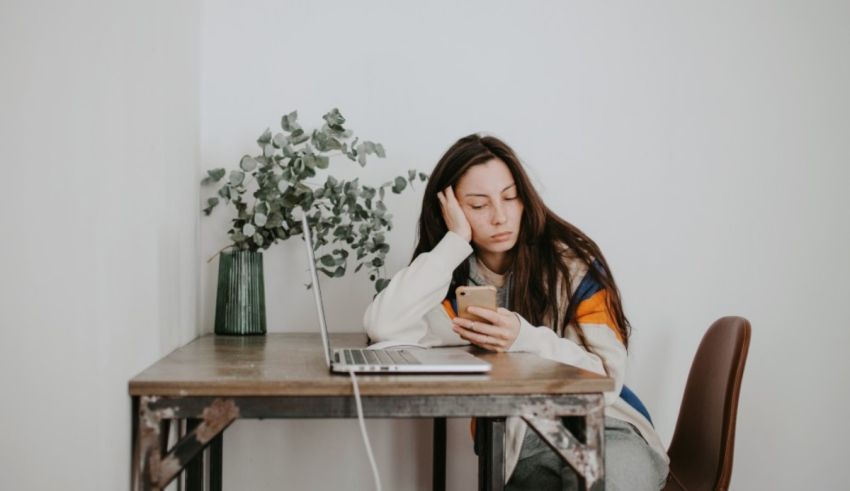 A woman sitting at a desk with a laptop and cell phone.