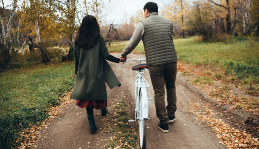 A couple is walking down a path with a bicycle.