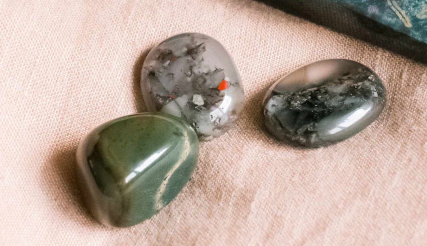 Three green and black stones on a table next to a book.