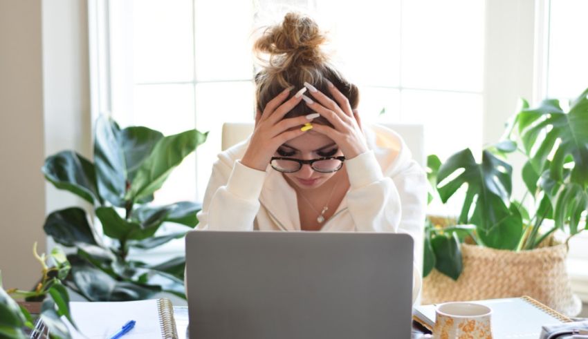 A woman is holding her head in front of her laptop.