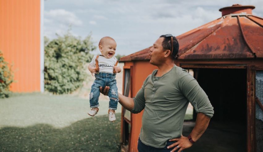 A man holding a baby in front of a barn.