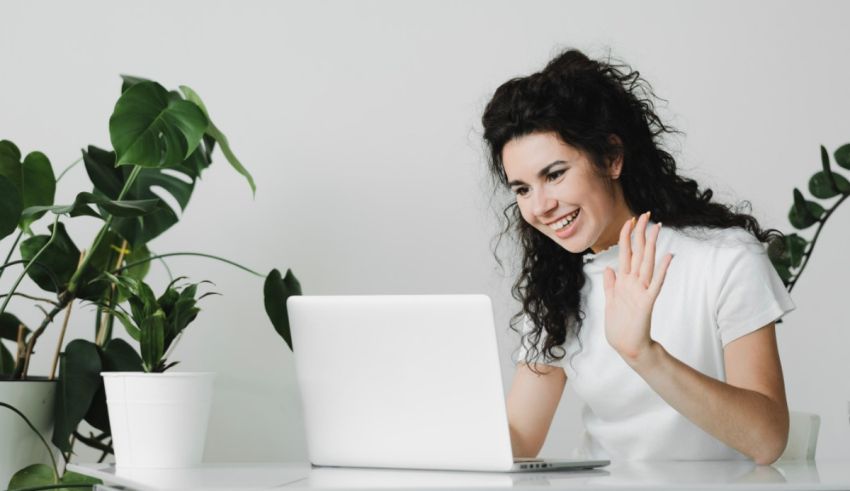 A woman is sitting at a desk with a laptop and a plant in front of her.
